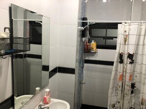 A bathroom with a white sink, a mirror, a shower with a curtain, and toiletries on a shelf. - Den Nest Guest House KRABI (Krabi)
