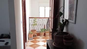 Un couloir menant à un balcon agrémenté de plantes en pot et doté d’un sol à carreaux.