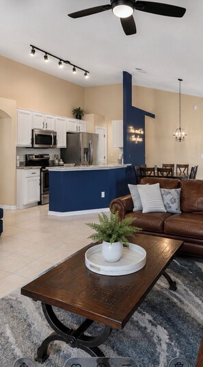 A modern living room with a brown leather sofa, a coffee table with a plant, and a dining area with wooden chairs.