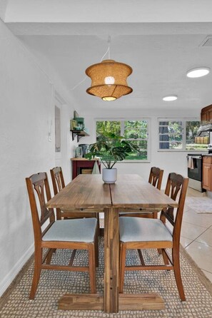 A dining area with a wooden table and chairs, a hanging light fixture, and a view of the outdoors through a window. - ParkView Palms, Mid-Century Home, Sleeps 6, Pets (Mount Dora)