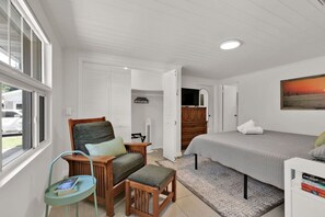 A bedroom with a bed, a chair, a small table, a TV, and a painting on the wall. - ParkView Palms, Mid-Century Home, Sleeps 6, Pets (Mount Dora)