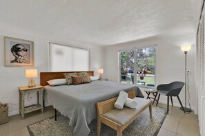 A bedroom with a bed, bedside tables, a bench, a chair, and a window with a view of the outside. - ParkView Palms, Mid-Century Home, Sleeps 6, Pets (Mount Dora)