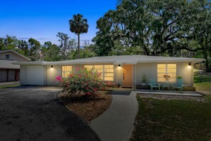 A single-story house with a garage, a front porch with a table and chairs, and a well-maintained lawn. - ParkView Palms, Mid-Century Home, Sleeps 6, Pets (Mount Dora)