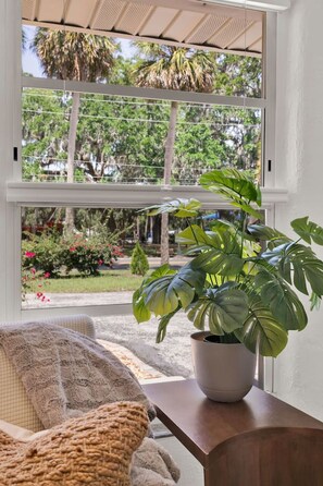 A room with a large window, a potted plant, a cushioned chair, and a wooden table. - ParkView Palms, Mid-Century Home, Sleeps 6, Pets (Mount Dora)
