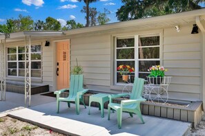 A single-story house with a porch, a door, and a window with flowers. - ParkView Palms, Mid-Century Home, Sleeps 6, Pets (Mount Dora)