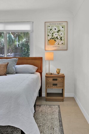 A bedroom with a bed, a nightstand, a lamp, a framed picture, and a window with a view of greenery. - ParkView Palms, Mid-Century Home, Sleeps 6, Pets (Mount Dora)