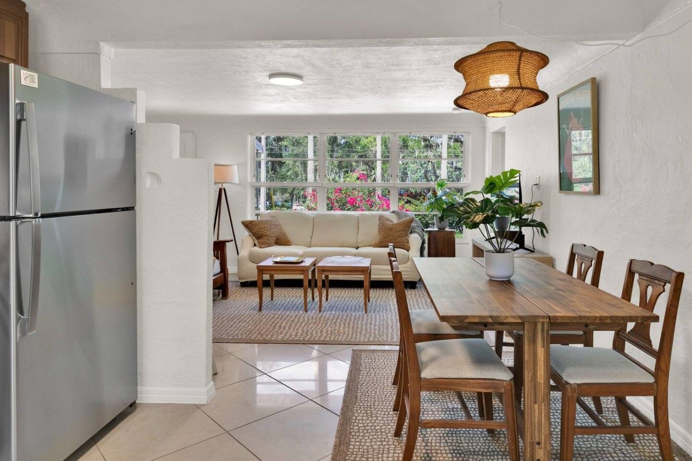 Una cocina con refrigerador, una mesa de comedor con sillas, un sofá y un ventanal con vista a la vegetación.
