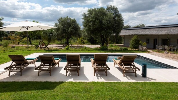 A pool with lounge chairs, a covered umbrella, and a building in the background. - Casa de Palmeiros Wellness & Pool Villa (Loulé)