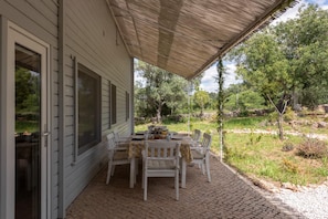 Un patio techado con mesa y sillas, vistas del paisaje circundante y un edificio con amplias ventanas.