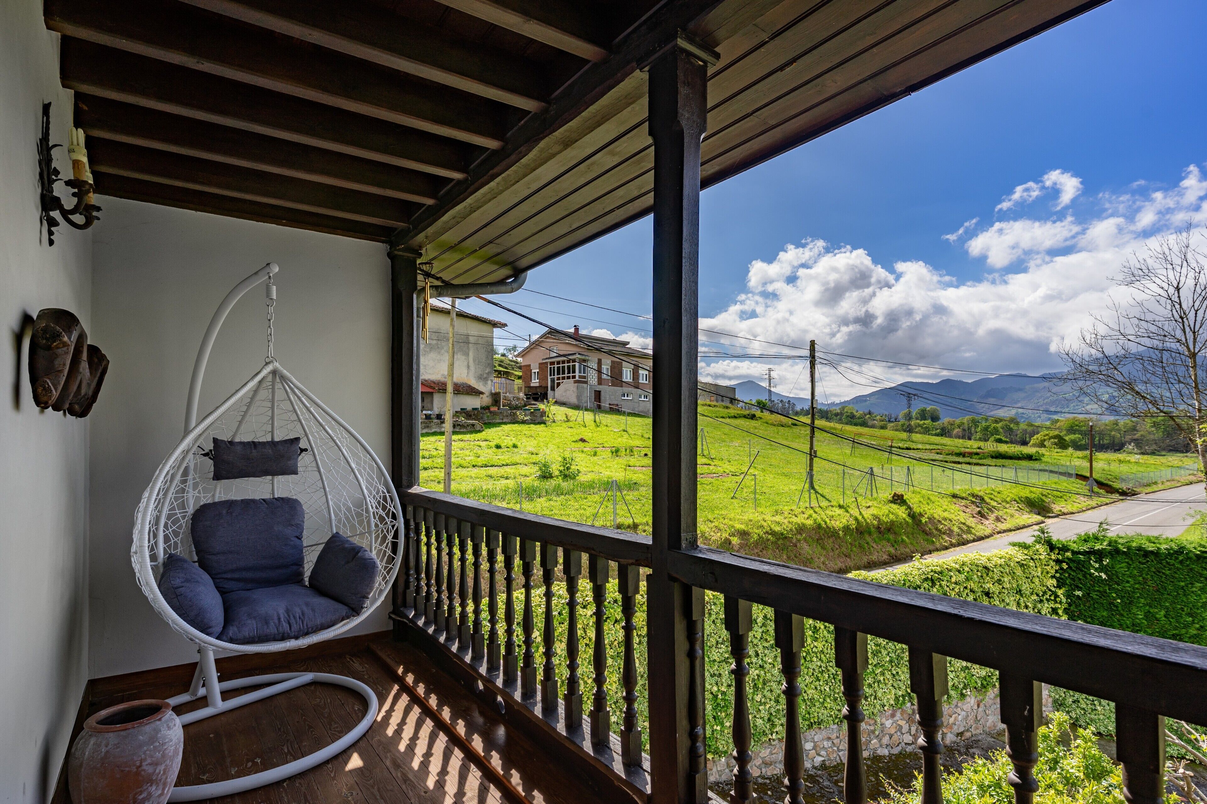 A room with a hanging chair, a rustic wooden ceiling, and a view of a green landscape with houses.