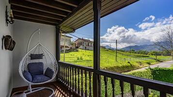 A room with a hanging chair, a rustic wooden ceiling, and a view of a green landscape with houses.