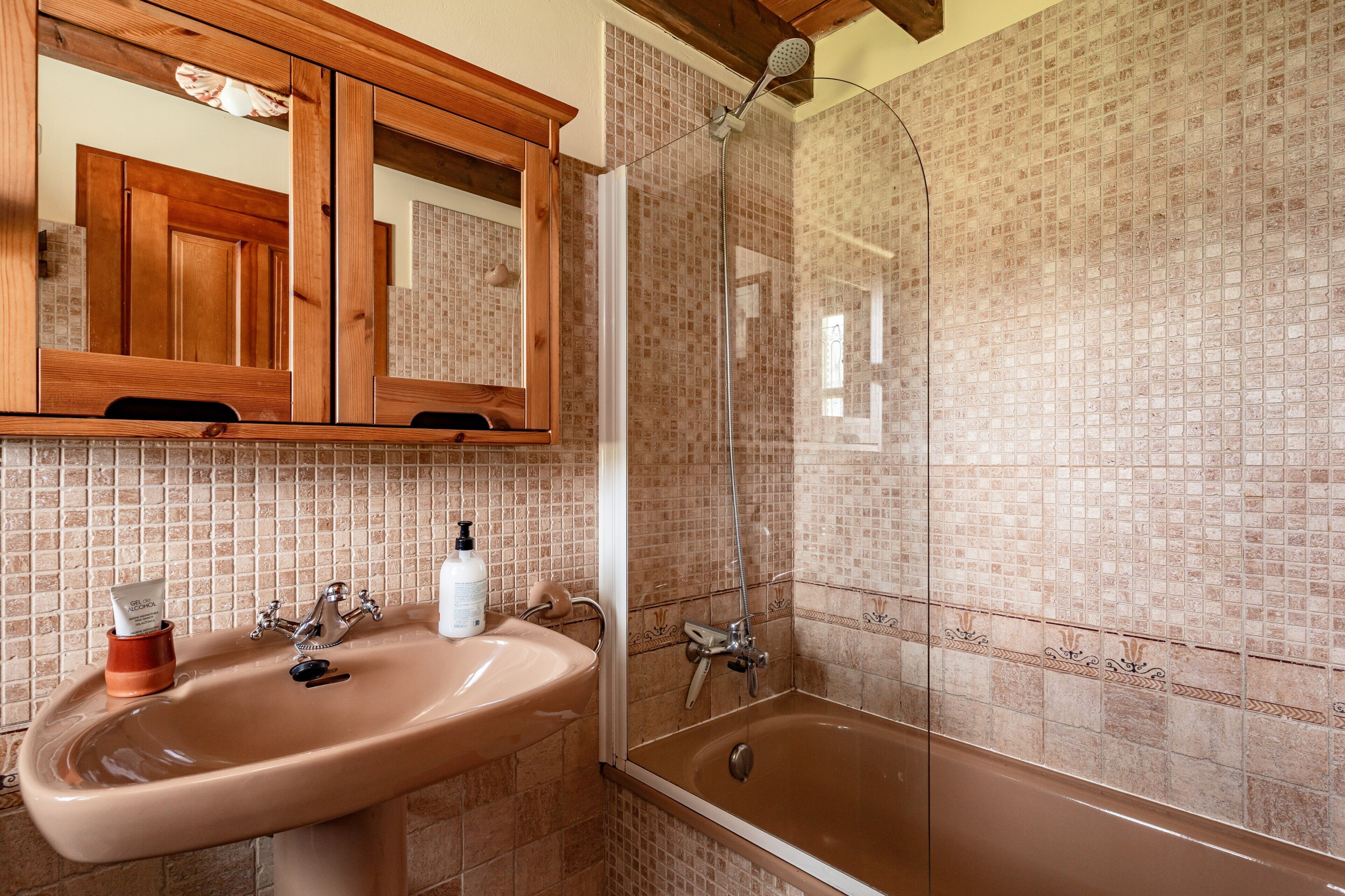 Un baño con lavamanos, espejo, ducha y paredes de azulejos.