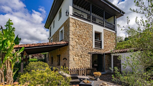A two-story stone house with a balcony, a covered patio, and a garden area.