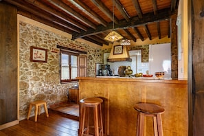 Una cocina rústica con paredes de piedra, vigas de madera, una zona de bar con taburetes y una chimenea de piedra.
