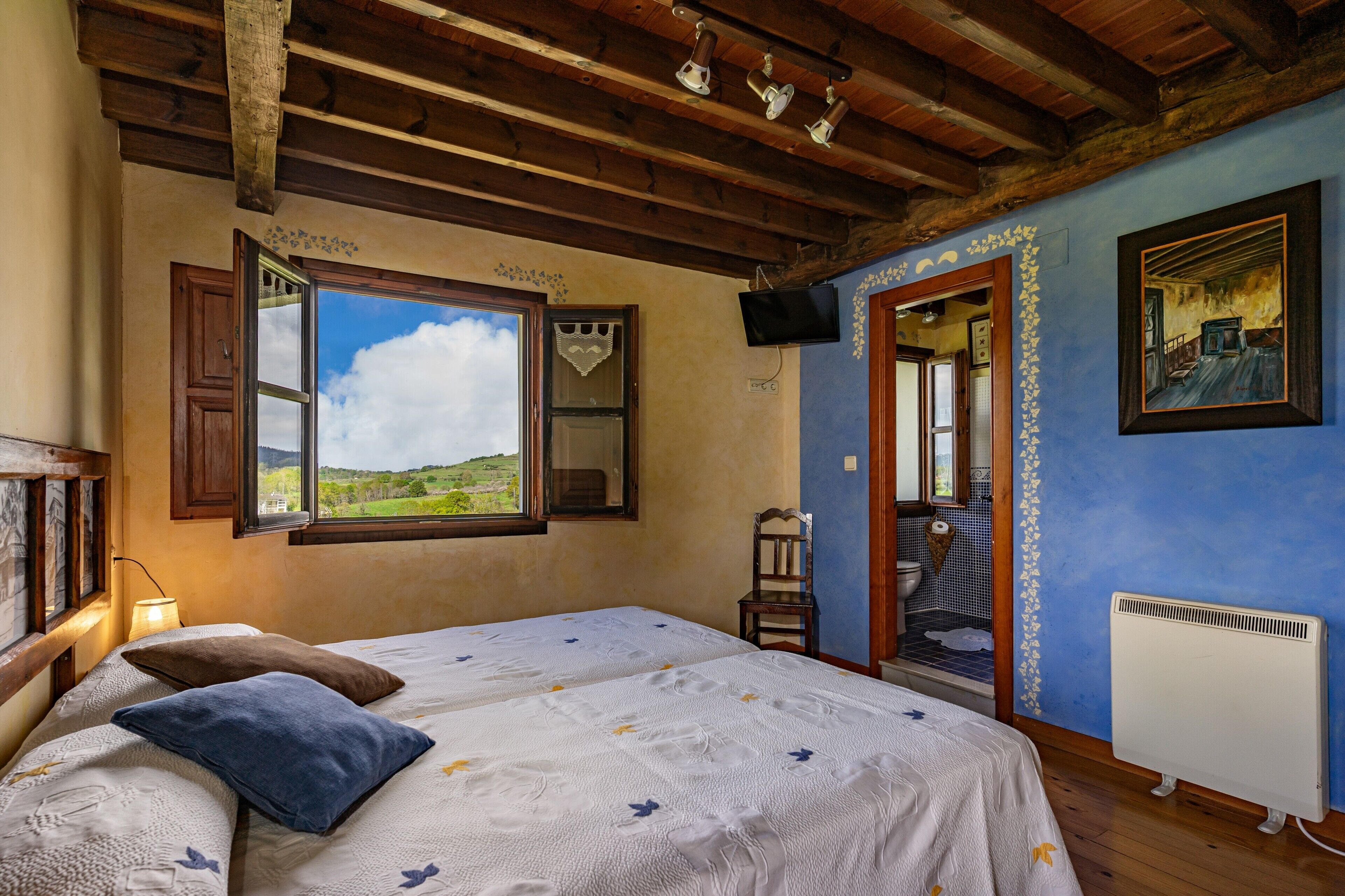 A bedroom with a large bed, a window with an open door, a radiator, and a television on the wall.