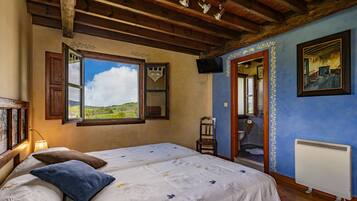 A bedroom with a large bed, a window with an open door, a radiator, and a television on the wall.