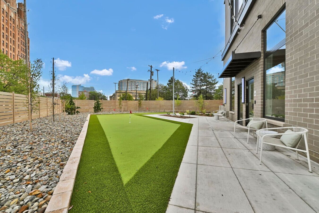 A modern outdoor area with a putting green, seating, and a building with large windows.
