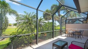A glass-enclosed balcony with outdoor furniture, palm trees, and a clear view of the surrounding landscape.
