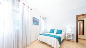 A neatly arranged bedroom with a bed, curtains, a bedside table, and a wall-mounted picture. - El Charco Azul (San Andrés y Sauces)
