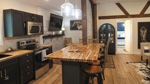 Una cucina moderna con mobili scuri, un'isola in legno e una TV a parete.