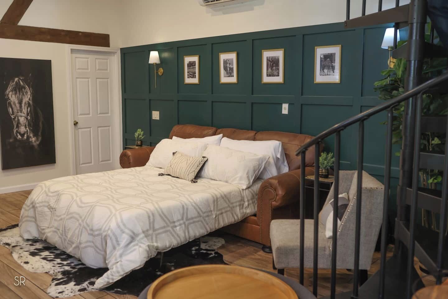 Een slaapkamer met een bed, een stoel, een trap en een muur met ingelijste foto's.