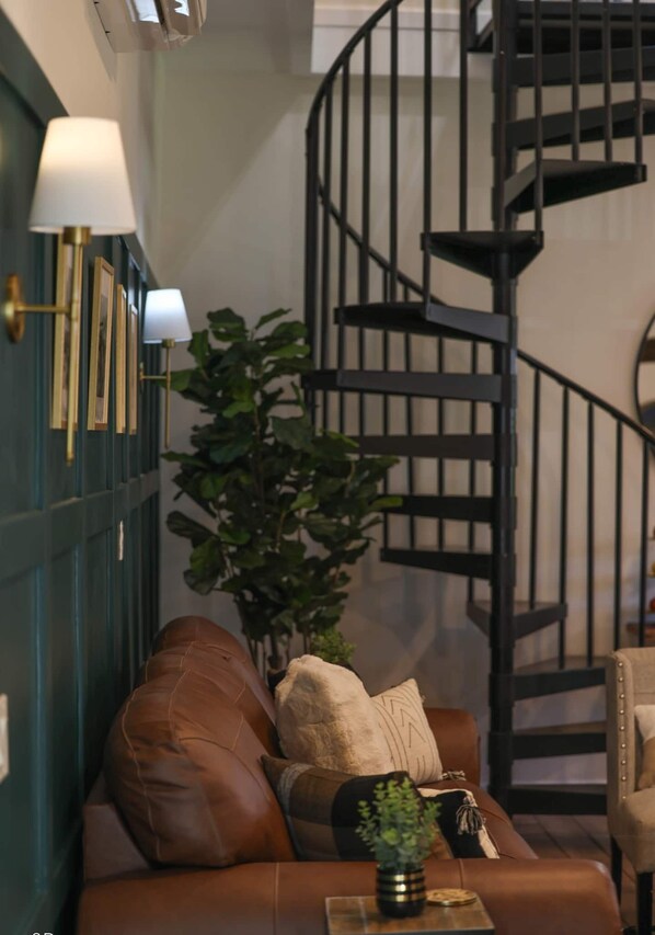 A cozy living room with a brown leather sofa, a potted plant, and a spiral staircase. - The Horse Carriage 2 miles from Foxwoods Casino (Preston)
