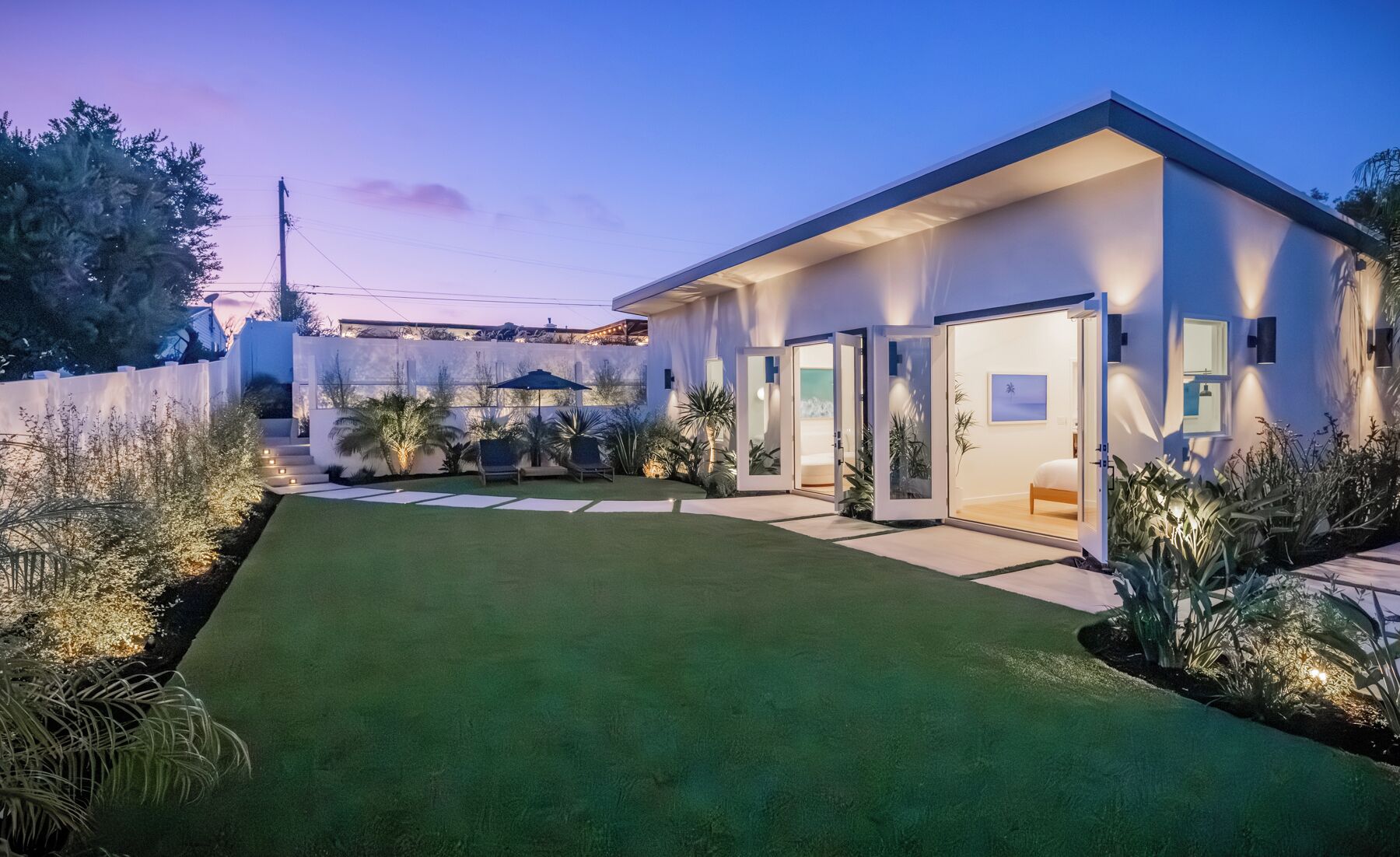 A modern house with a well-maintained lawn, a patio area, and a bedroom visible through an open door.