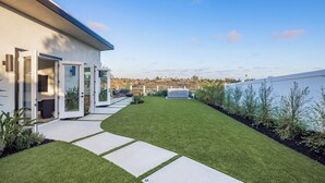 Una casa moderna con un césped cuidado, un patio con mobiliario exterior y una vista despejada del paisaje circundante.