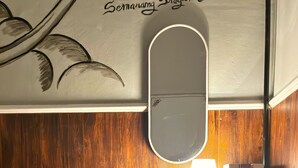 A room with a wooden wall, a mirror, a table with a lamp, and books on a shelf. - Semarang Co Stay (Semarang)