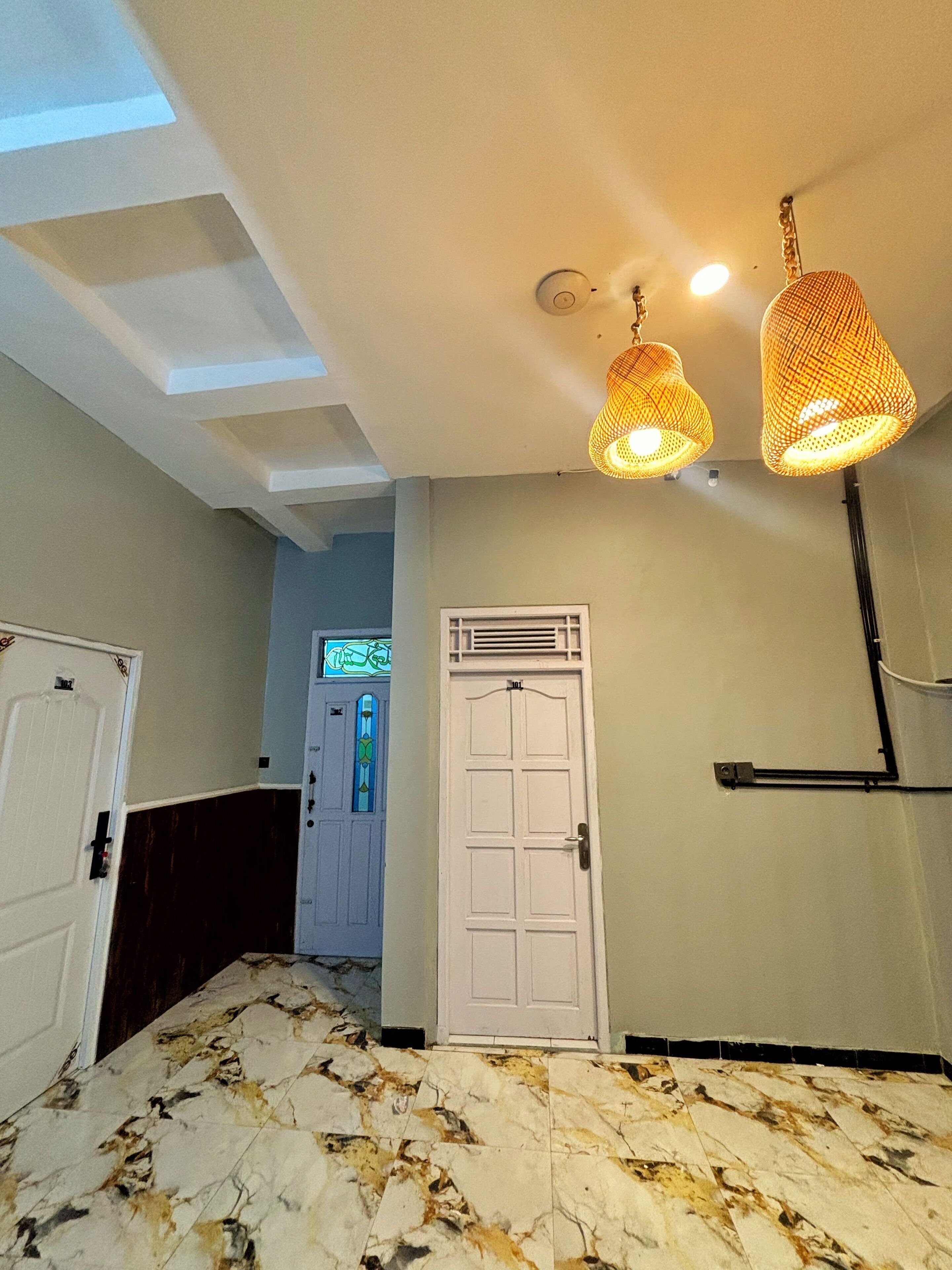 Quarto de hotel com piso de mármore, porta branca e duas luminárias pendentes.