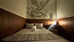A bedroom with a wooden headboard, a bed with patterned pillows, a decorative wall mural of a dragon, and a bedside lamp.