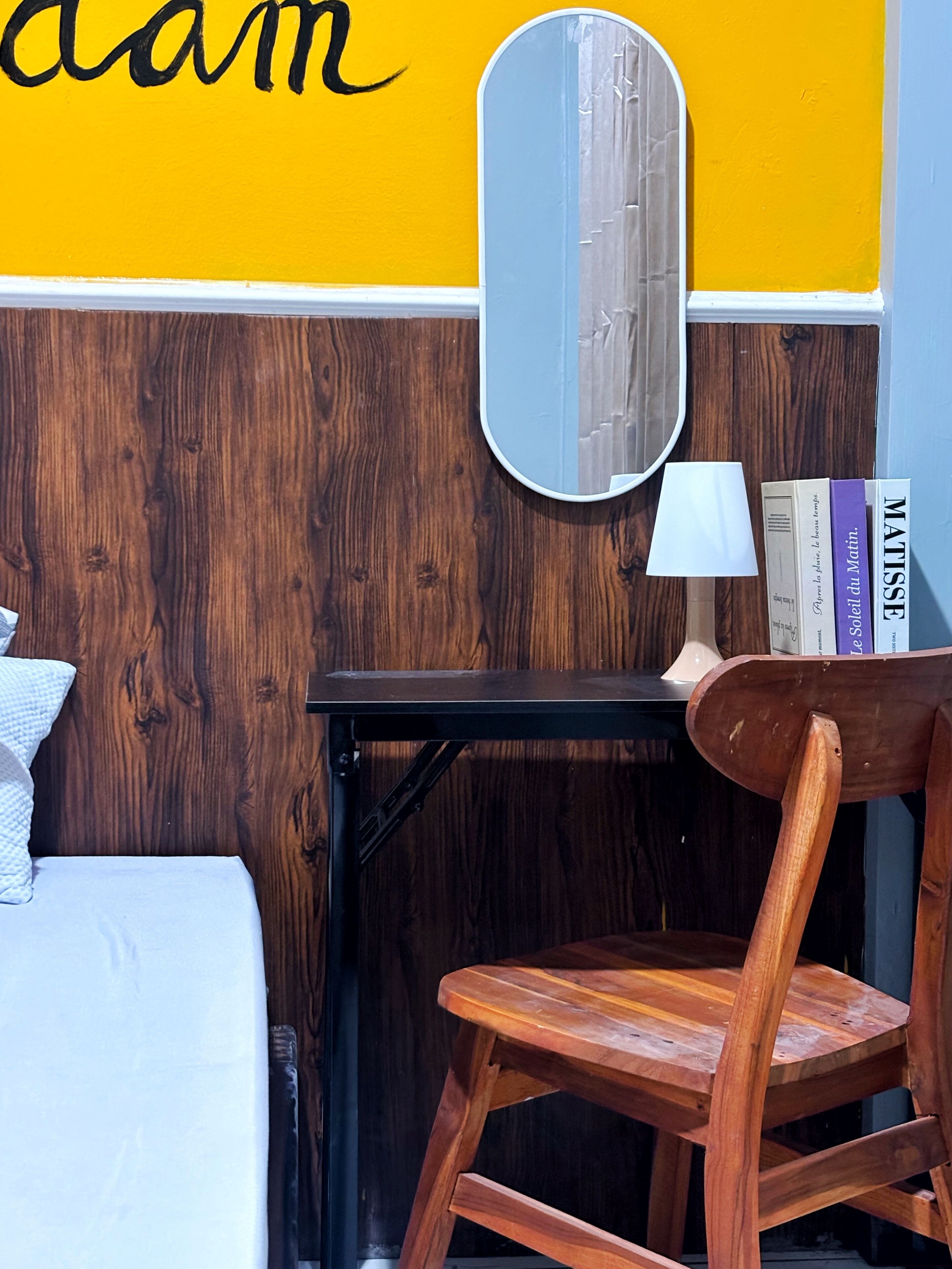 Una stanza con un letto, una sedia in legno, un tavolino, uno specchio e una parete con decorazioni giallo e blu.