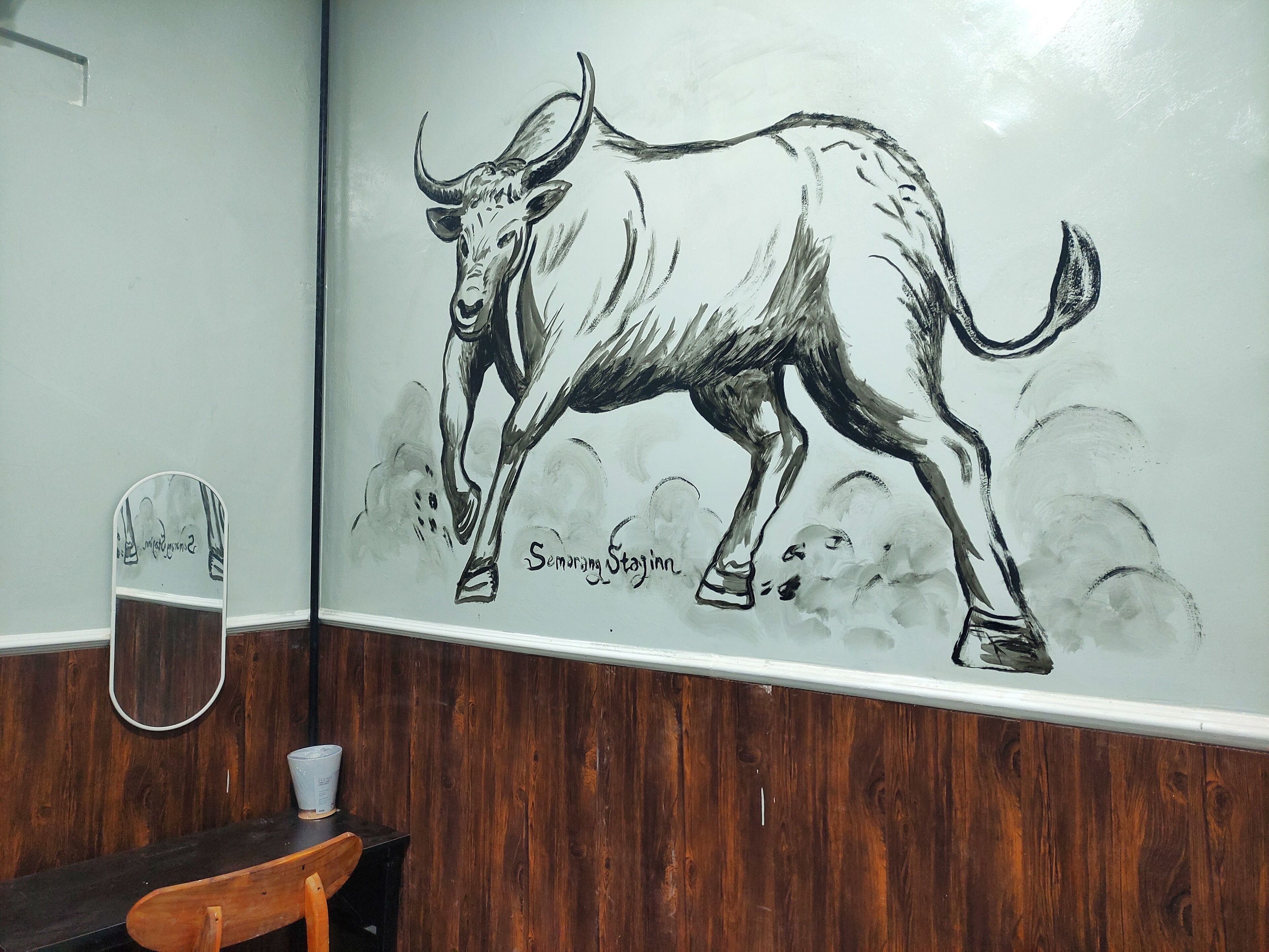 A wall mural of a bull, a wooden bench, and a small table with a cup.