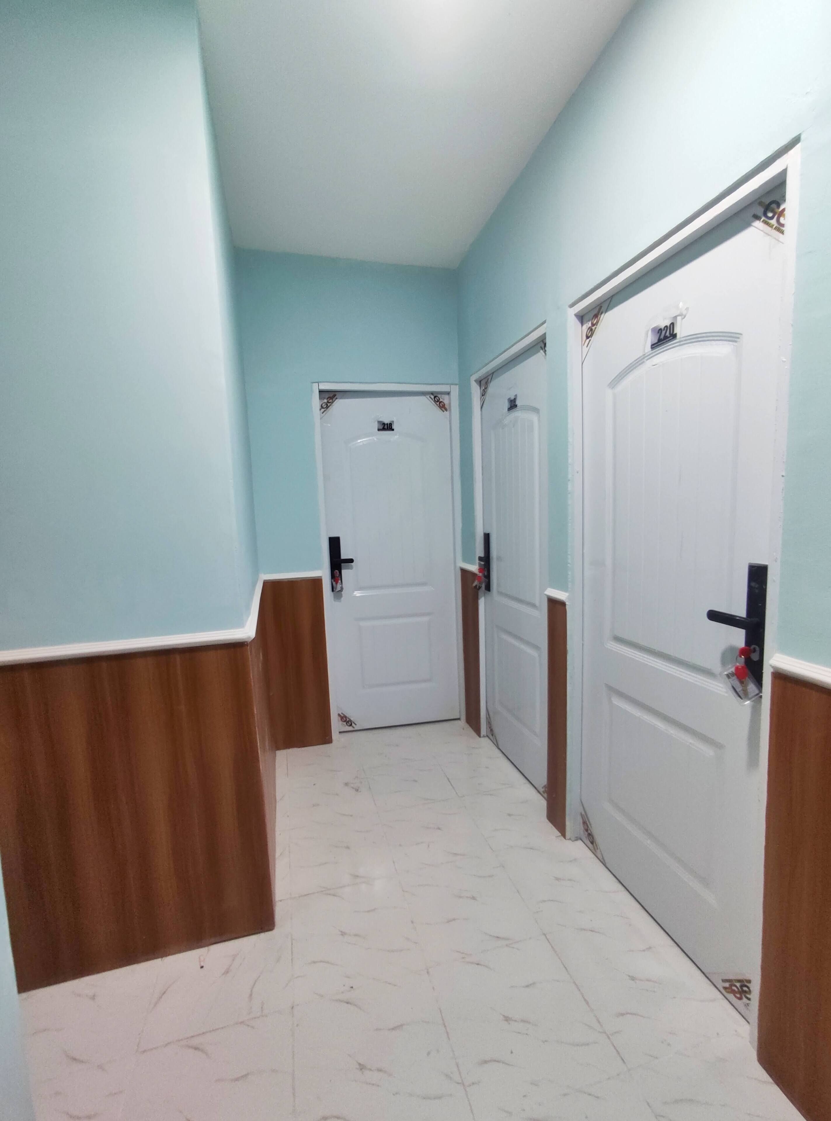 Um corredor com duas portas brancas, cada uma delas numerada. As paredes estão pintadas de azul claro e o chão é ladrilhado.