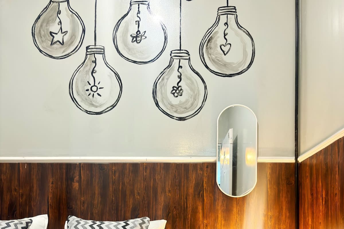 A bedroom with a bed, pillows, a bedside table with a lamp, and a wall with light bulb decorations.