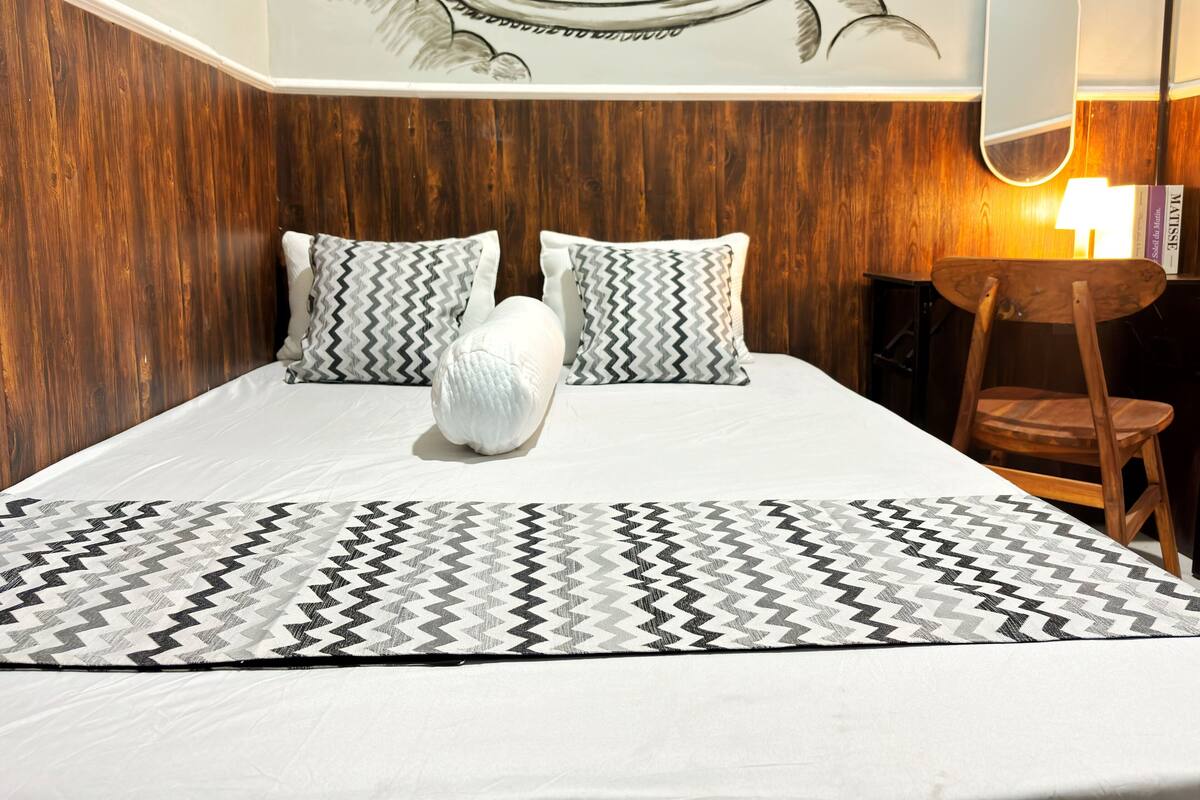 A neatly made bed with a patterned bedspread, two pillows with a zigzag design, and a wooden headboard.