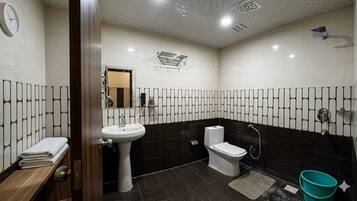 Un baño con lavabo, inodoro y ducha. Hay un perchero y un espejo.