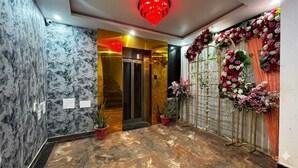 A marble-floored lobby with a red light fixture, a glass elevator, and floral decorations. - Hotel Kings Paradise & Banquet (Lucknow)
