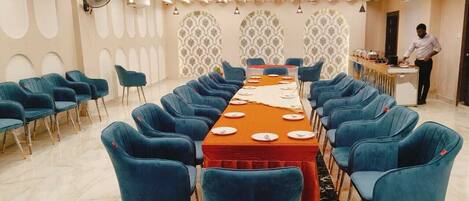 Ein Konferenzraum mit einem langen Tisch, blauen Stühlen und einer Person, die an einem Buffet steht.