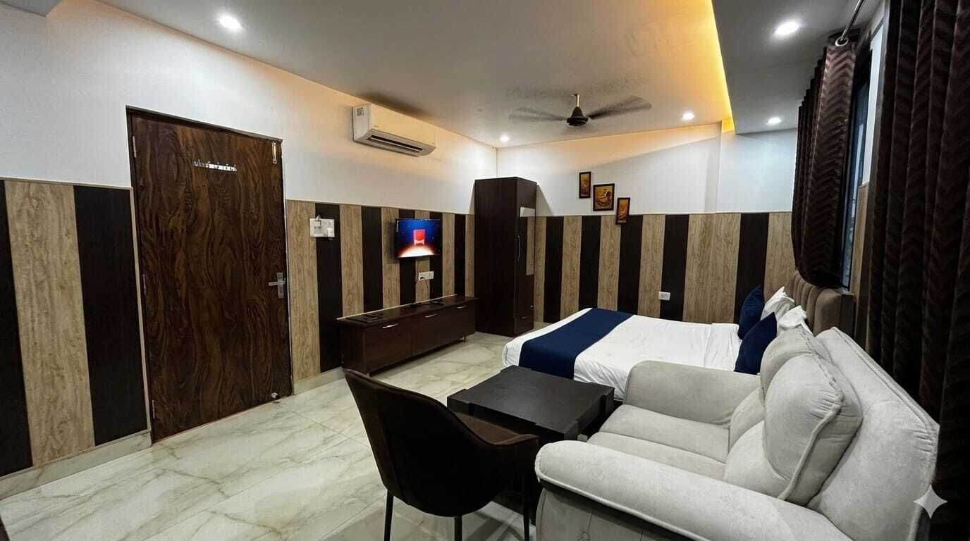Une chambre d’hôtel avec un lit, un canapé, un bureau et une chaise. Il y a un téléviseur au mur et un ventilateur de plafond.
