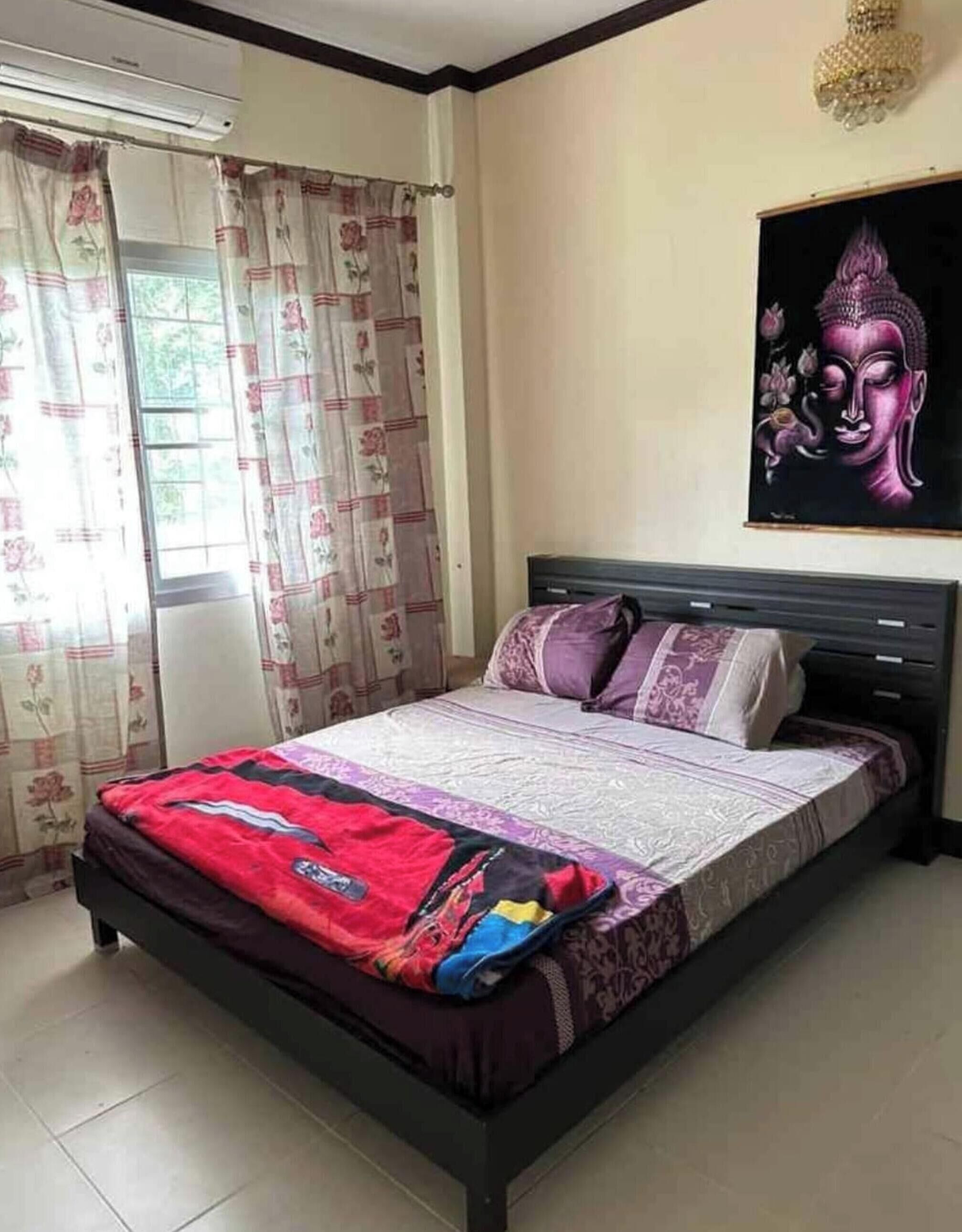 A bedroom with a bed, curtains, a wall-mounted Buddha painting, and a ceiling light fixture.