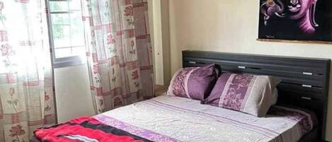 A bedroom with a bed, curtains, a wall-mounted Buddha painting, and a ceiling light fixture.