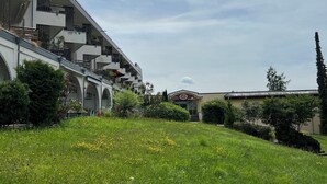 A modern building with multiple balconies and a grassy area with flowers. - Alpenruhe Vacation Rental with Exceptional Mountain Views, Pool, and Sauna (Scheidegg)