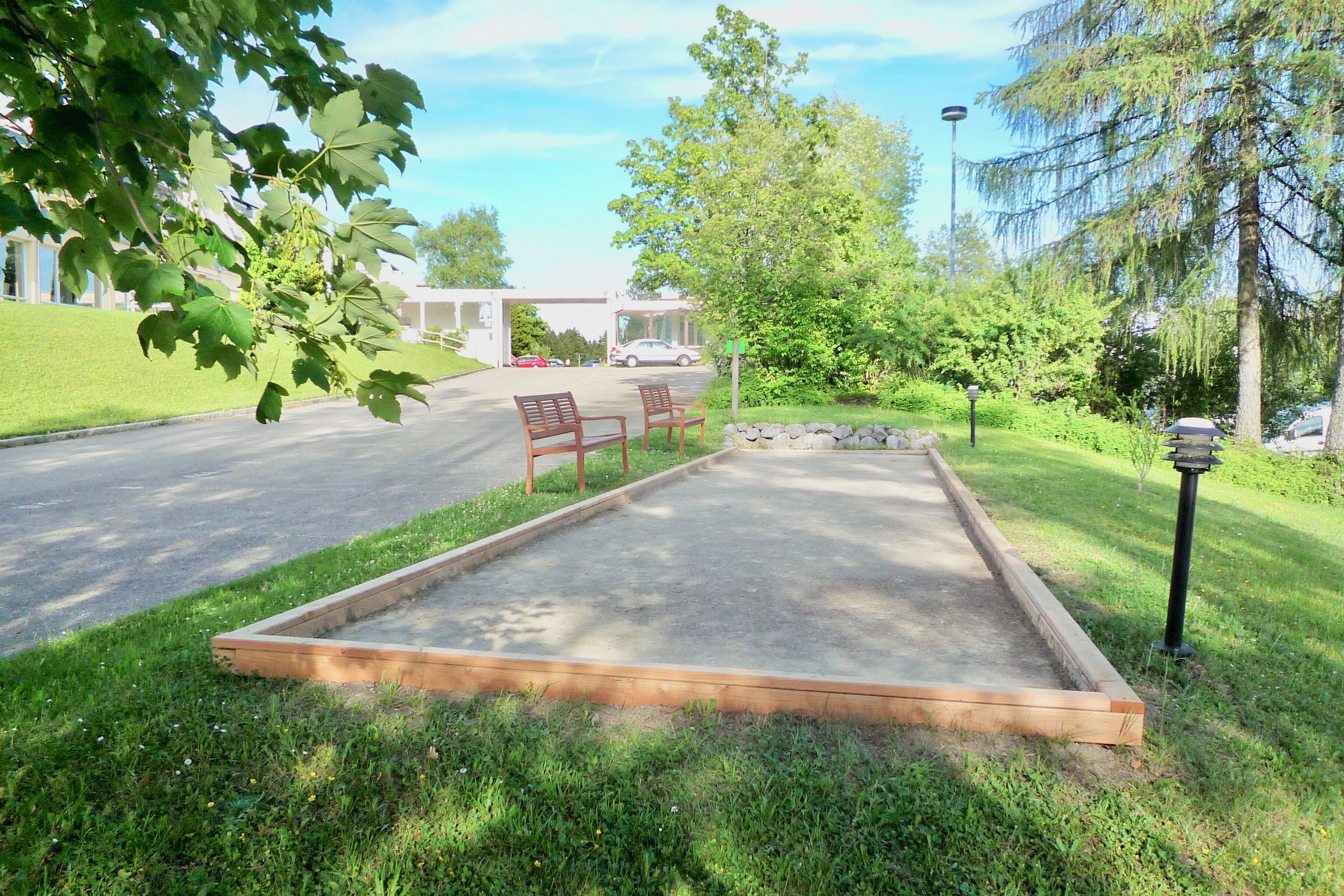 Une zone dallée avec deux bancs en bois et une bordure en pierre, entourée de pelouse et d’arbres.