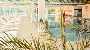 A pool area with lounge chairs, a pool with a blue and white checkered ceiling, and palm plants. - Alpenruhe Vacation Rental with Exceptional Mountain Views, Pool, and Sauna (Scheidegg)