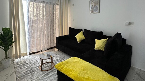 Un salon avec un canapé noir, un plaid jaune et un ventilateur de plafond.