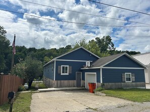 A two-story blue house with a front door, a basketball hoop, and a wooden fence.