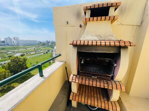 A balcony with a built-in brick oven, a railing, and a view of a cityscape.