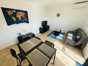 Ein Wohnzimmer mit Esstisch, Stühlen, einer Couch, einem Fernseher, einer Weltkarte an der Wand und einer Uhr.