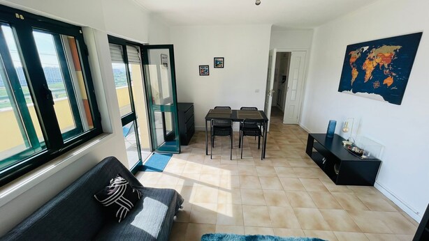 A living room with a sofa, a coffee table, a dining table with chairs, a TV stand, and a world map on the wall.